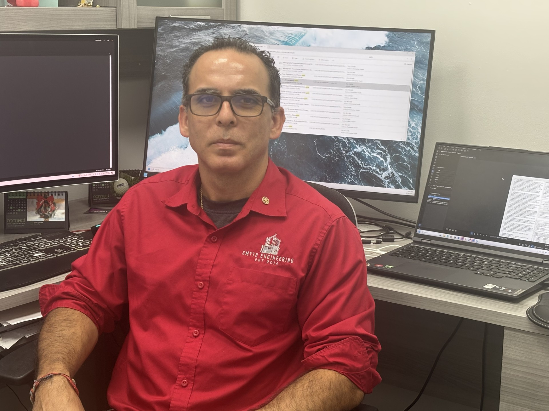 Man in red shirt using a drill on a window frame indoors.